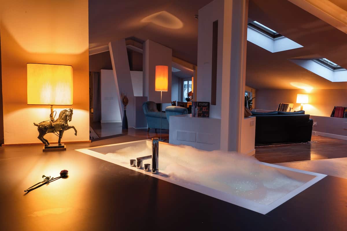A modern living room with a central white bathtub, a statue, and two lamps.