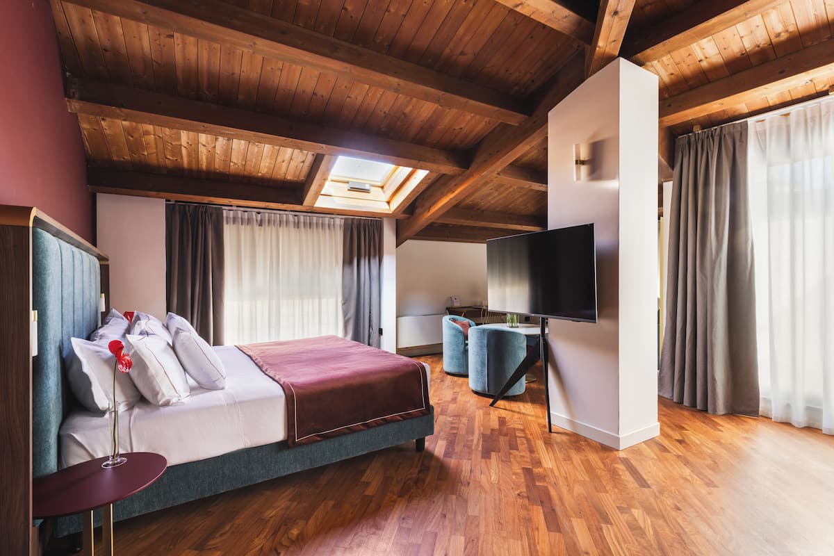 A modern hotel room with a wooden ceiling, a large bed, a flat-screen TV, and a skylight.