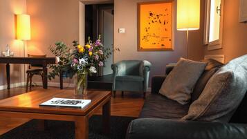 Una sala de estar con una mesa de centro de madera, un sofá, una silla, un jarrón con flores, una lámpara y un cuadro en la pared.