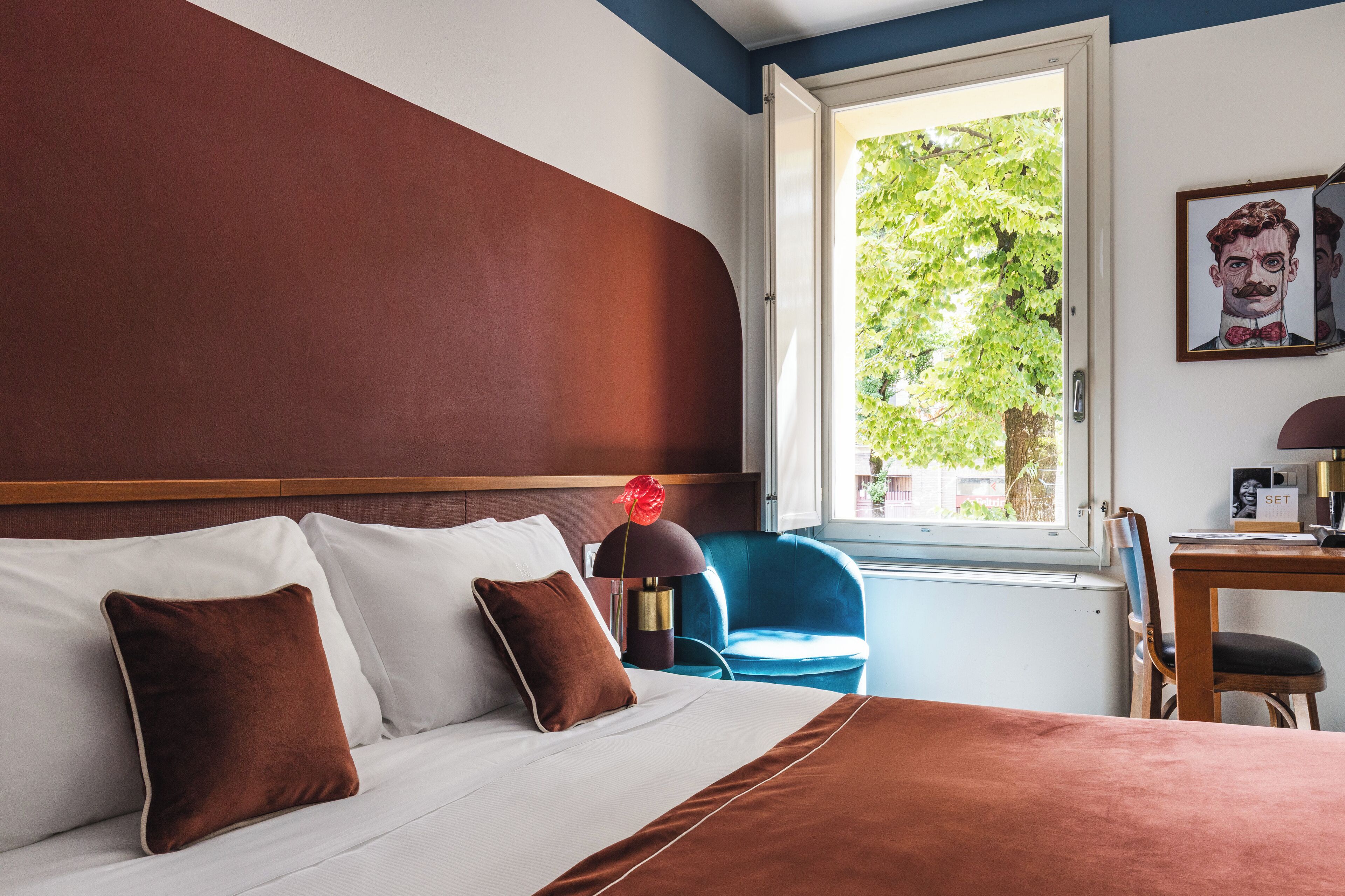 Une chambre d’hôtel avec un lit, un bureau, une chaise et une fenêtre donnant sur des arbres.