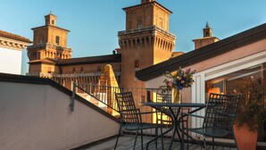A balcony with a table and chairs, overlooking a historic building with towers. - Casa d'Este - Hotel Ferrara (Ferrara)