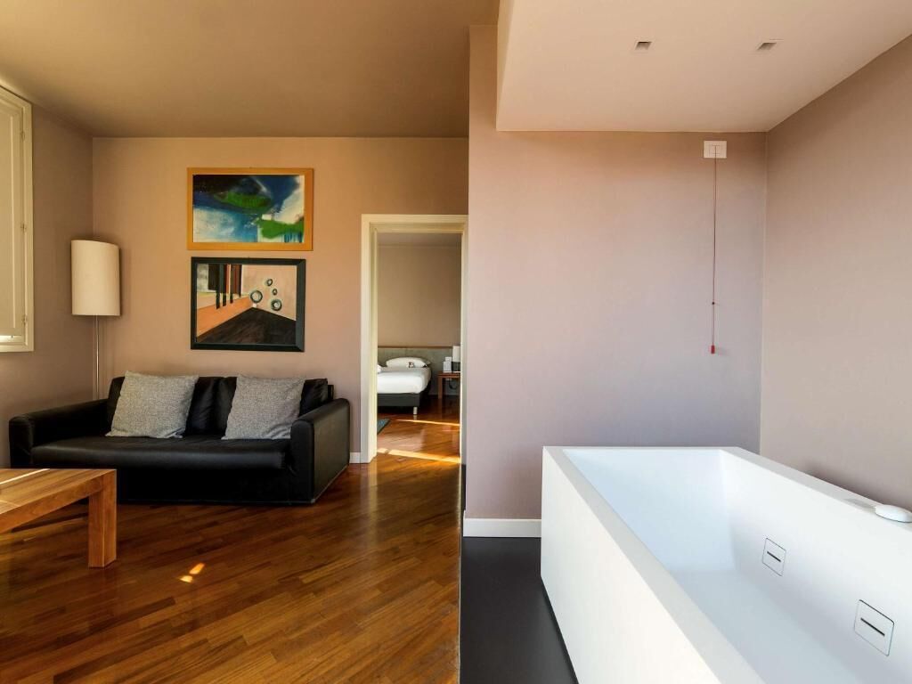 A modern living room with a black leather sofa, wooden coffee table, and a white bathtub.