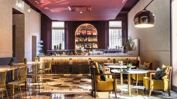 A bar area with a marble floor, seating with cushions, and a bar counter with a variety of bottles.