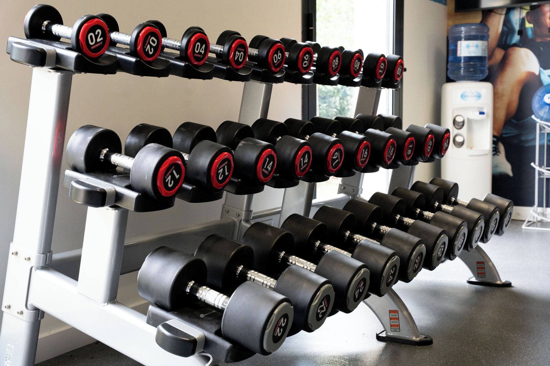 A weightlifting rack with multiple sets of dumbbells arranged in rows.