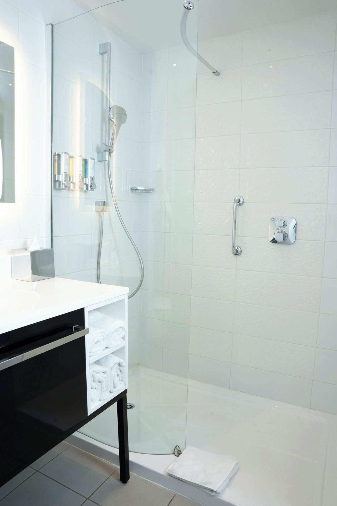 A modern bathroom with a glass-enclosed shower, a white vanity with a black cabinet, and a large mirror.