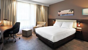 Una habitación de hotel con una cama grande, un escritorio, una silla y un pequeño reposapiés.