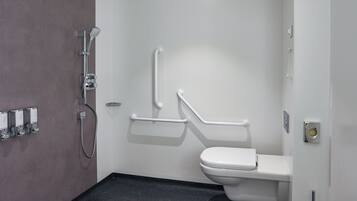 Un baño con inodoro blanco, ducha con cabezal de ducha manual y barra de apoyo.