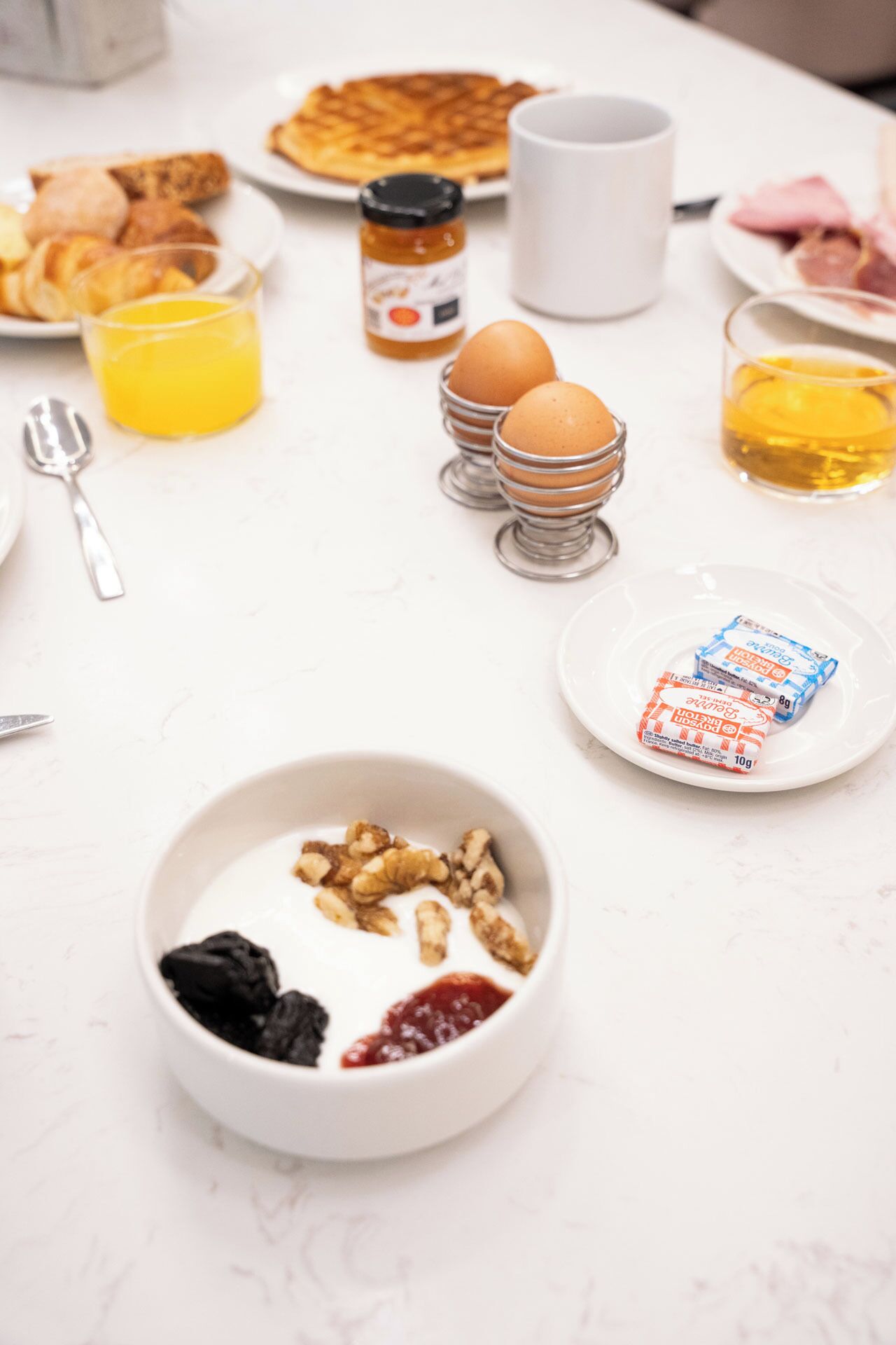 A breakfast table with various food items, including eggs, a bowl of yogurt with fruits, and a plate of pastries.