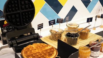 Un appareil à gaufres, avec des gaufres et divers accompagnements, posé sur un comptoir.