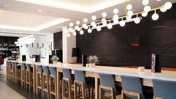 Un área de bar moderna con una barra larga, varios taburetes y una lámpara decorativa.