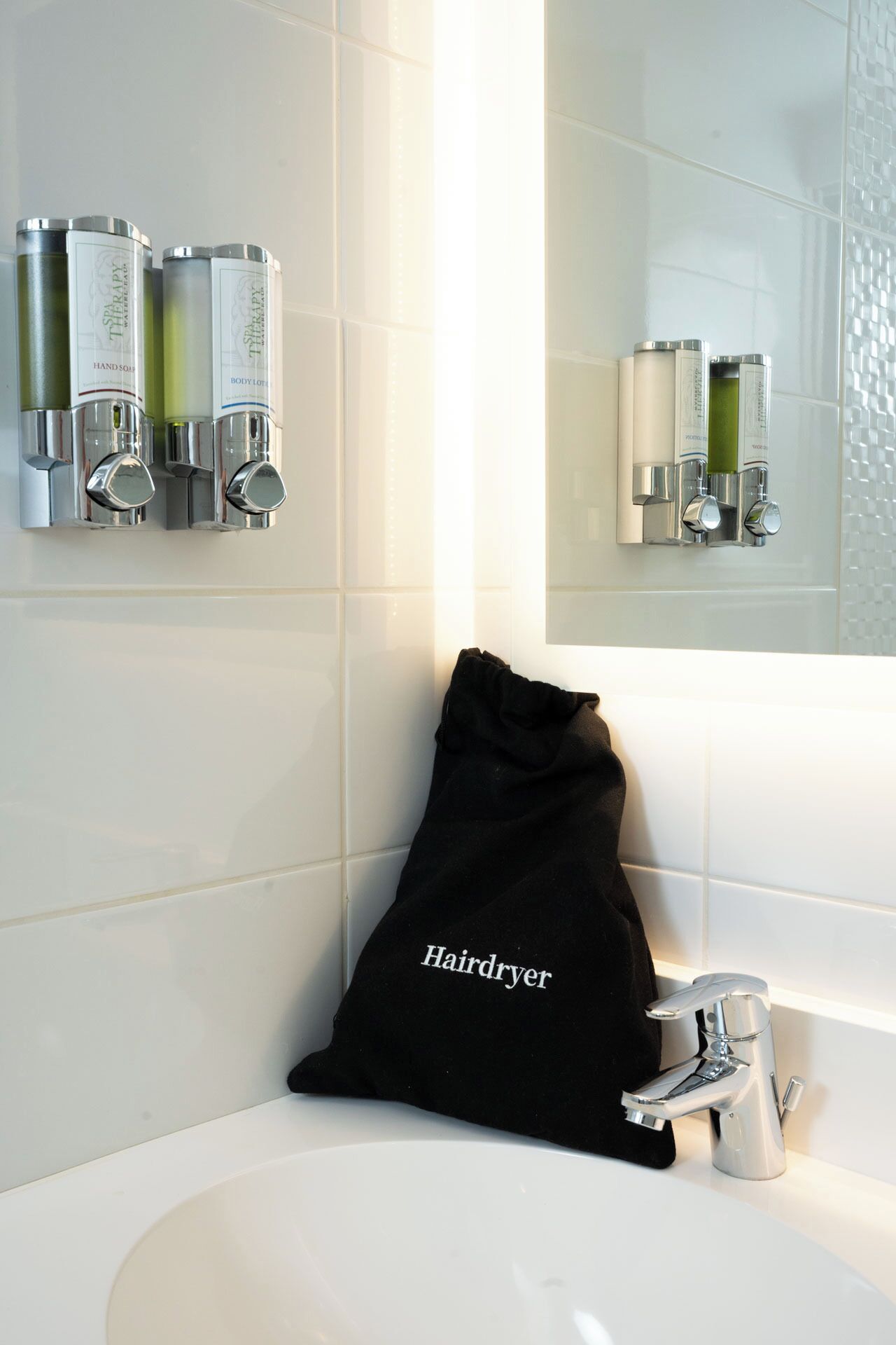 A bathroom with a white sink, a hairdryer, and toiletries on a wall-mounted dispenser.