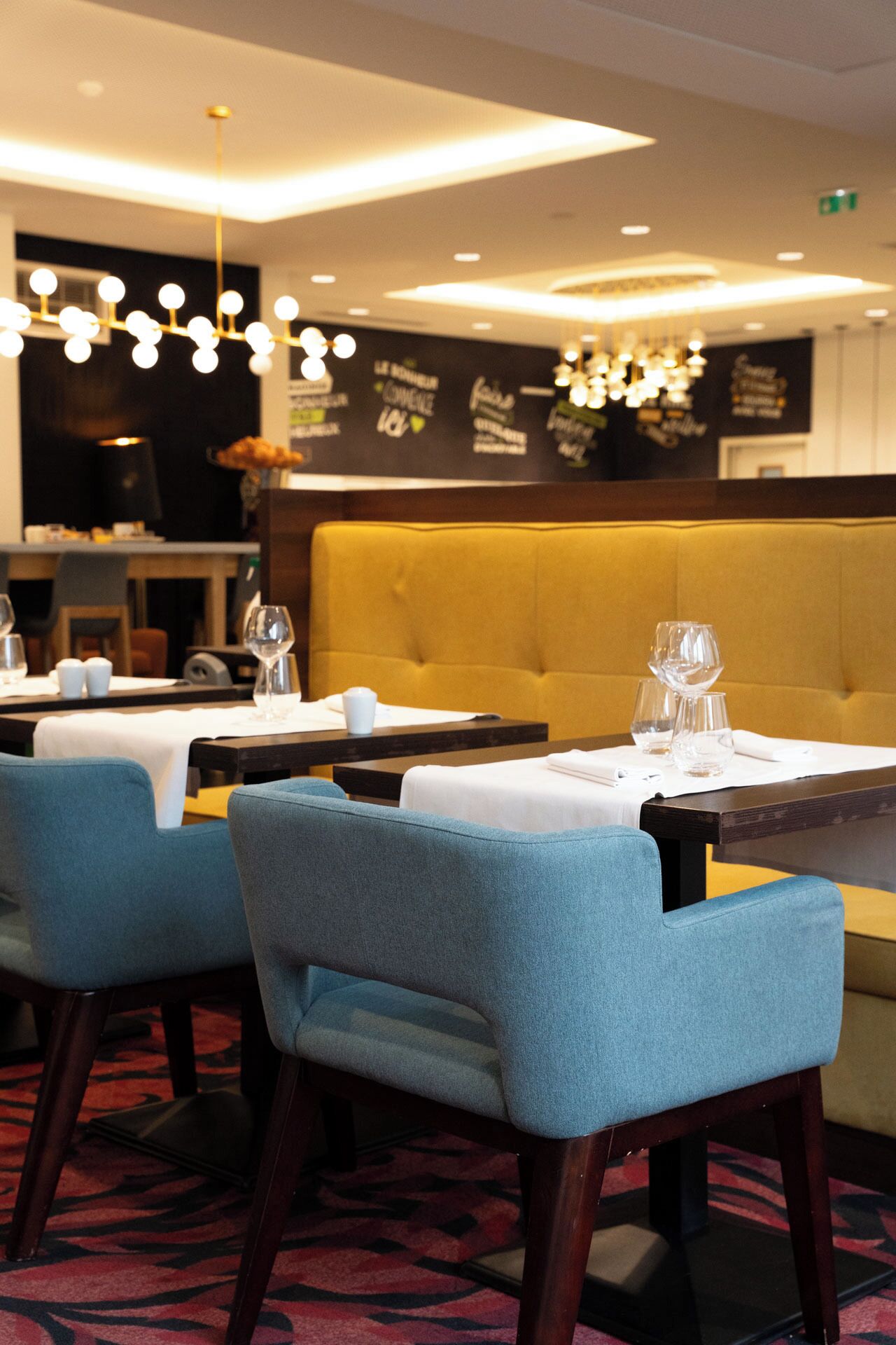 A restaurant interior with blue upholstered chairs, tables with white tablecloths, and hanging light fixtures.