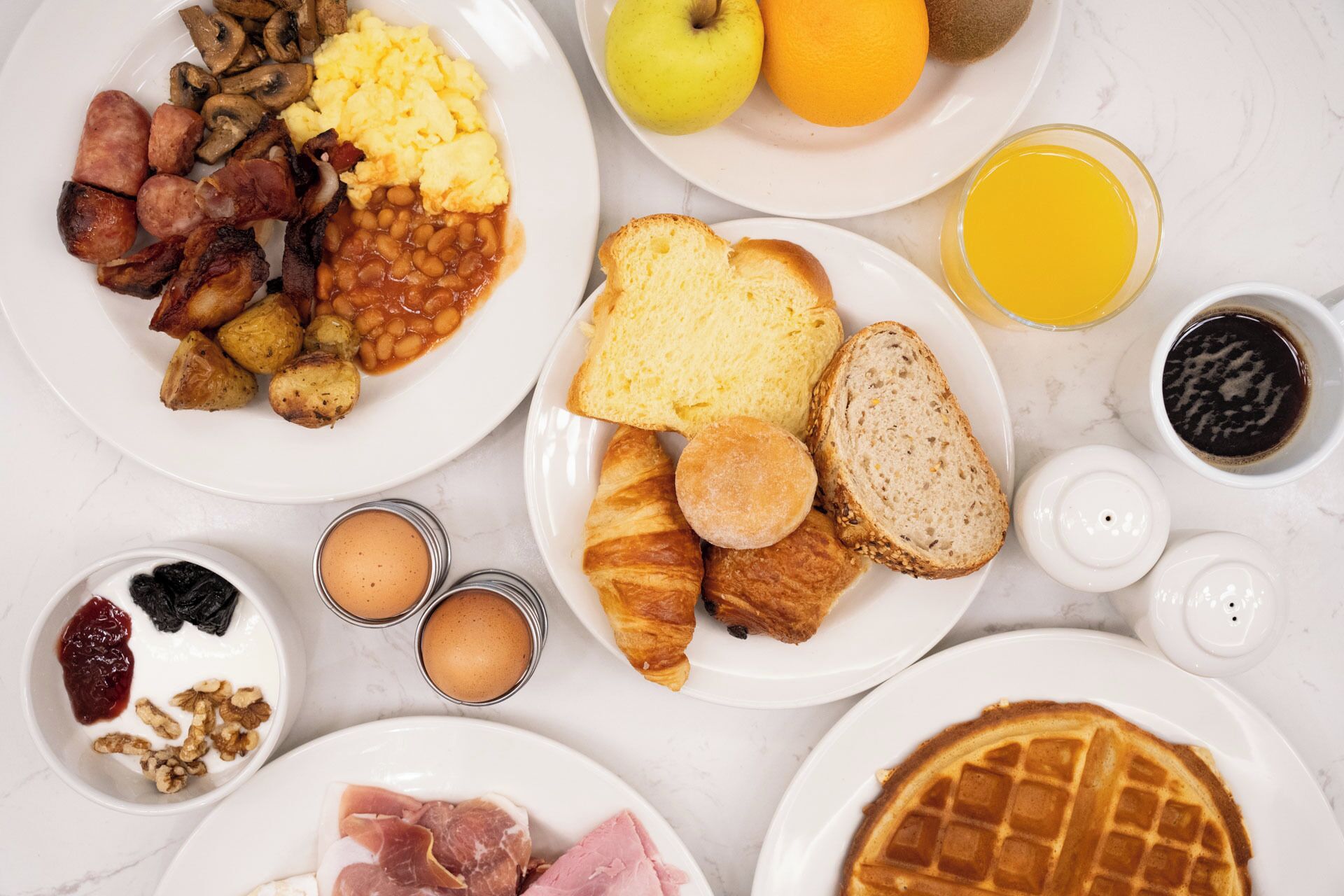 Uma mesa de café da manhã com diversos alimentos e bebidas em pratos.