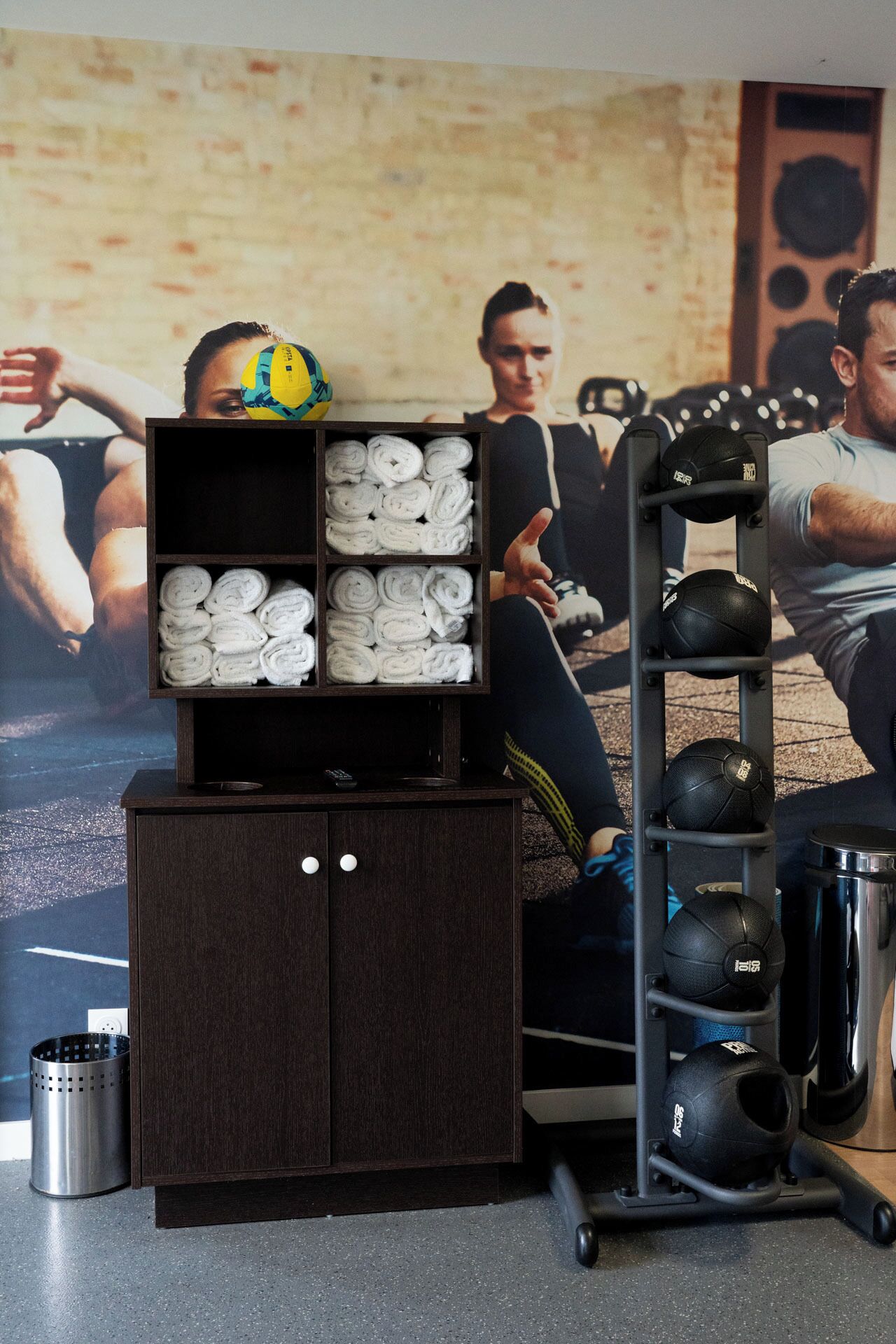 Un gimnasio con equipo de ejercicio, un estante con toallas y un cartel en el fondo.