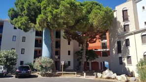 Un immeuble à plusieurs étages doté de balcons, d’un espace de stationnement et d’un grand arbre à l’avant.