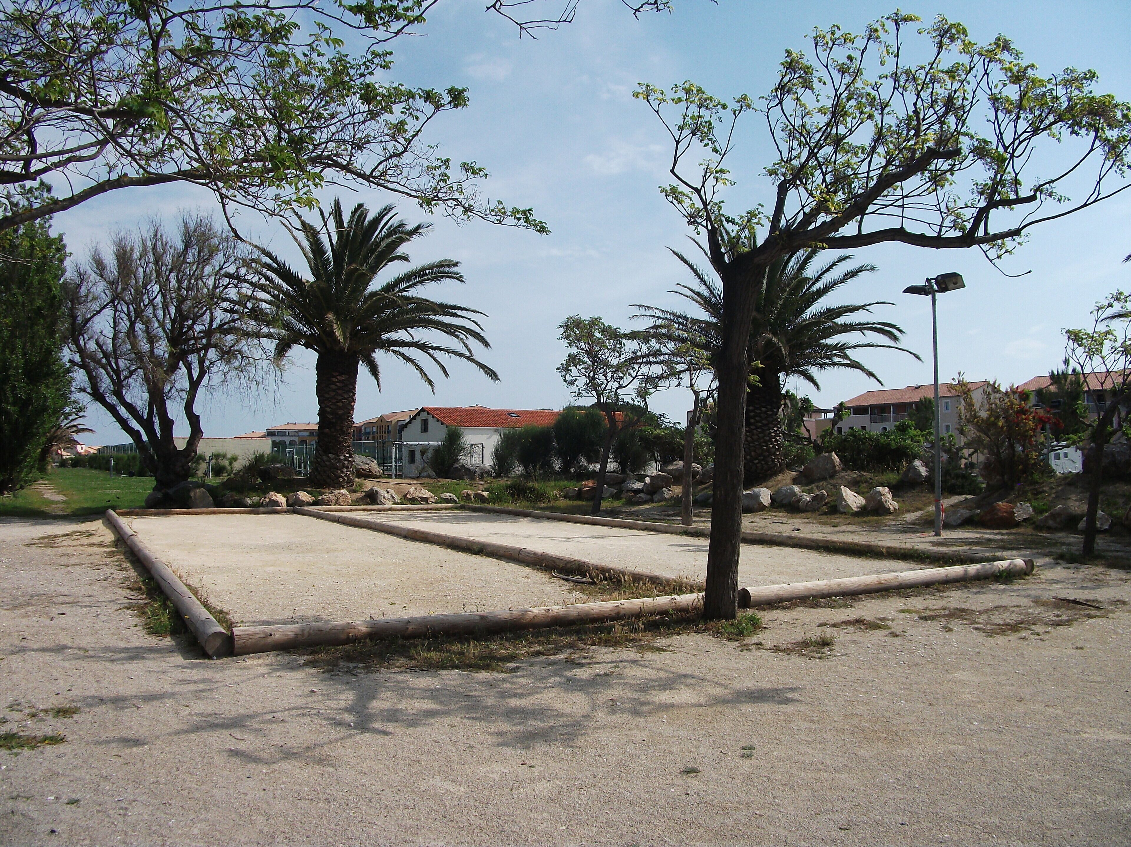 An outdoor area with a concrete play structure, palm trees, and a building in the background.