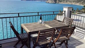 Una mesa y sillas de madera en un balcón con vistas al mar y a las montañas.