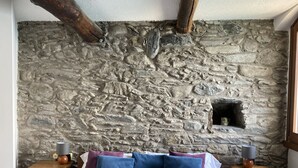 Un dormitorio con pared de piedra, cama con almohadas azules y púrpuras, mesitas de noche de madera y un pequeño estante.