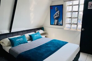Moderni hotellihuone, jossa on sänky, yöpöytä, juliste seinällä ja ikkuna, josta on näkymä ulos.