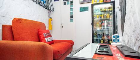 Una habitación con sofá rojo, una mesita de vidrio con un dispositivo Philips, un refrigerador lleno de bebidas y un perchero para bicicletas en la pared.