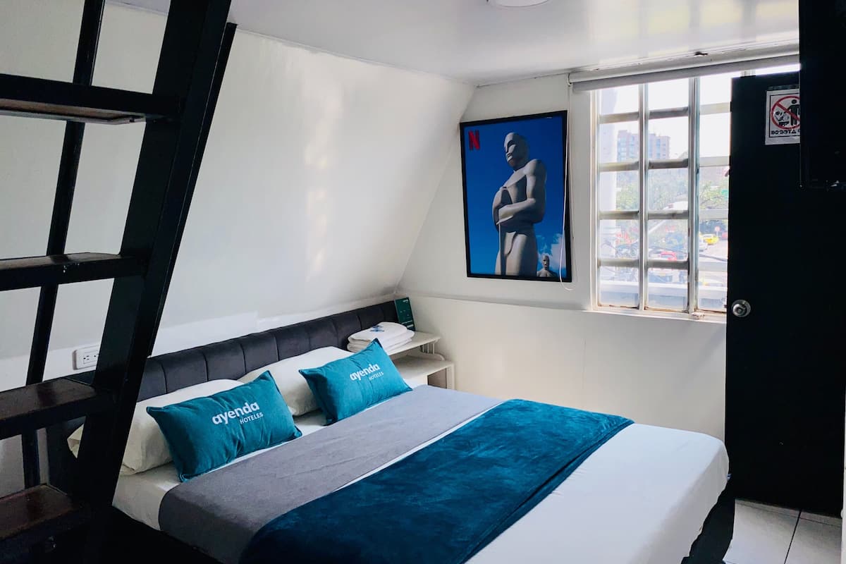 Una habitación de hotel con una cama, una ventana que ofrece vistas a la ciudad, una puerta y una obra de arte colgada en la pared.