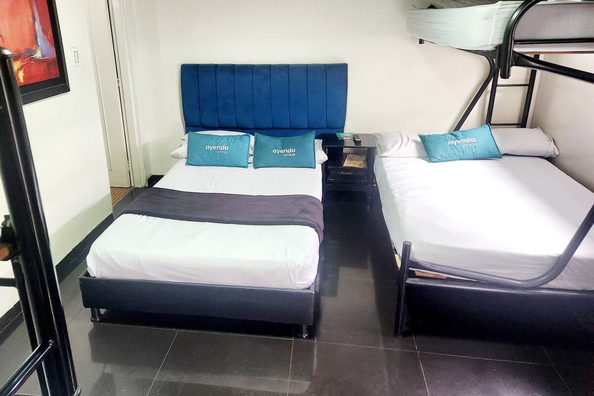 Habitación de hotel con dos camas, cada una con cabecera azul y almohadas a juego. Hay una mesita de noche con lámpara entre las camas.