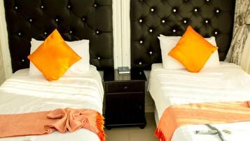 Habitación de hotel con dos camas, cada una con cabecero negro tapizado y ropa de cama blanca. Hay dos almohadas naranjas en cada cama.