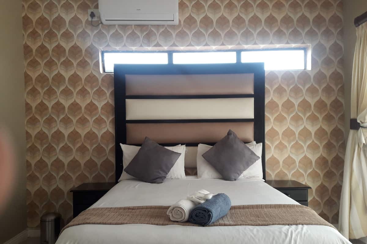 Een opgemaakt bed met hoofdbord, kussens en een opgerolde handdoek.
