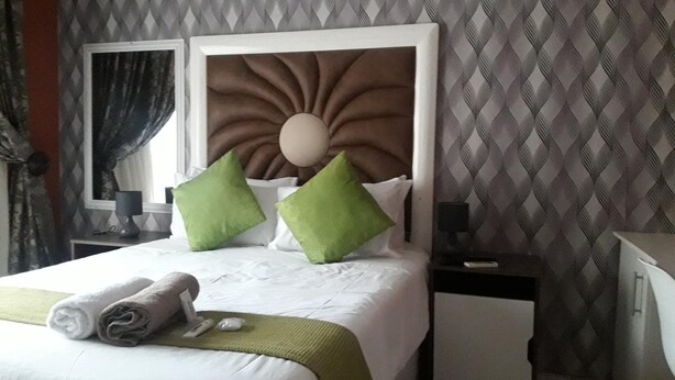 A neatly made bed with pillows, a bedside table with a lamp, and a wall with a geometric pattern.