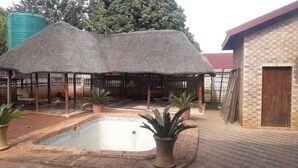 A covered outdoor area with a pool, potted plants, and a brick building.