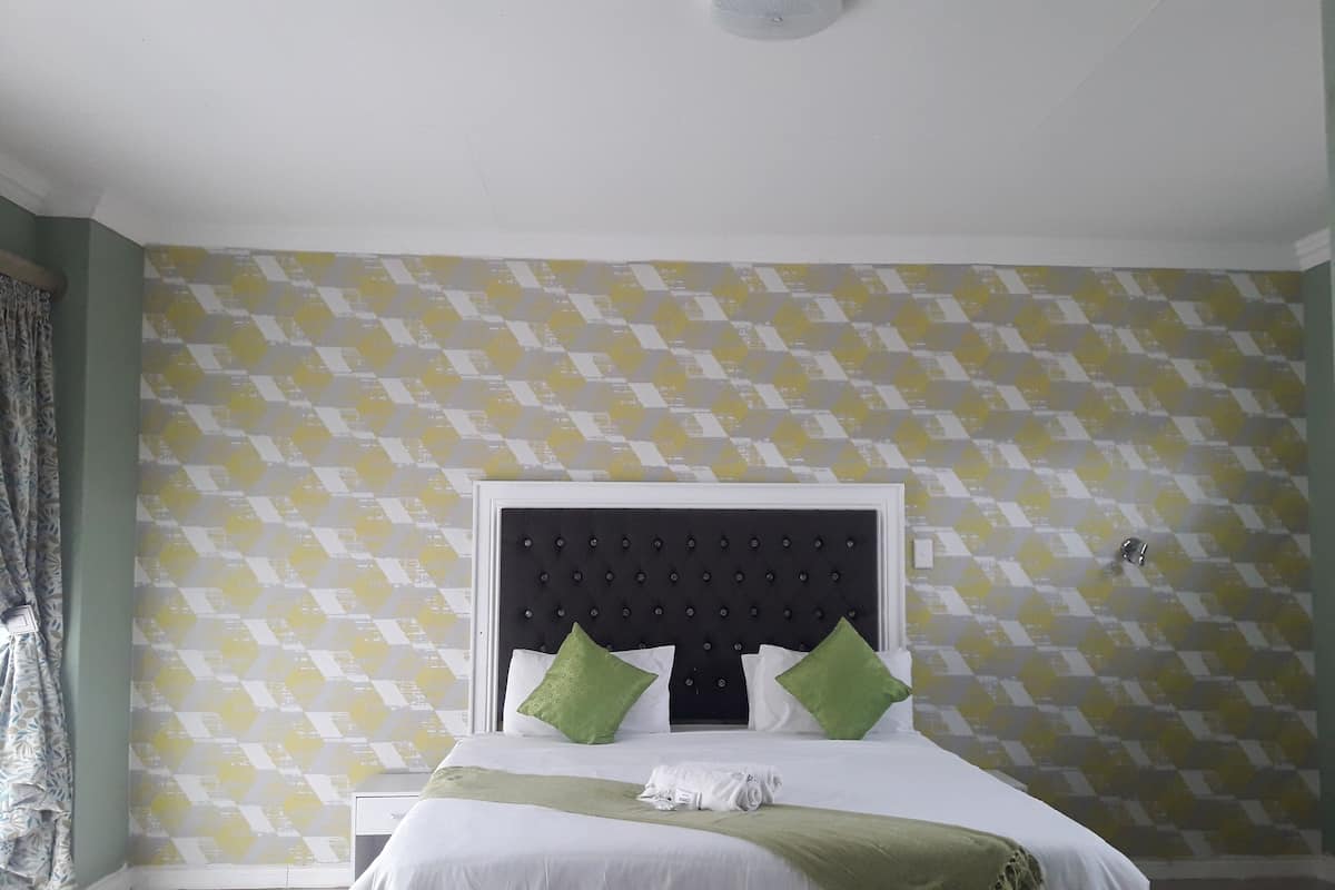 Een net opgemaakt bed met een wit en groen deken, twee groene kussens en een witte handdoek. De kamer heeft een muren met een geel en wit patroon en een witte hoofdbord.