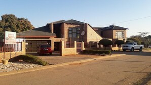 A two-story building with a garage, a red car parked in front, and a white pickup truck parked on the street.