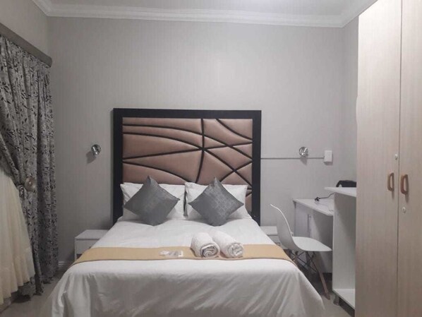 A neatly made bed with a headboard, two pillows, and rolled towels on the bed.