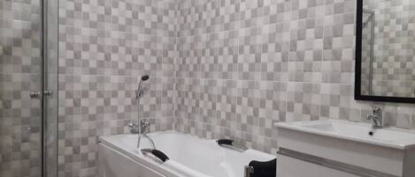 Un baño moderno con pared de baldosas a cuadros, cabina de ducha de vidrio, bañera independiente y tocador con espejo.