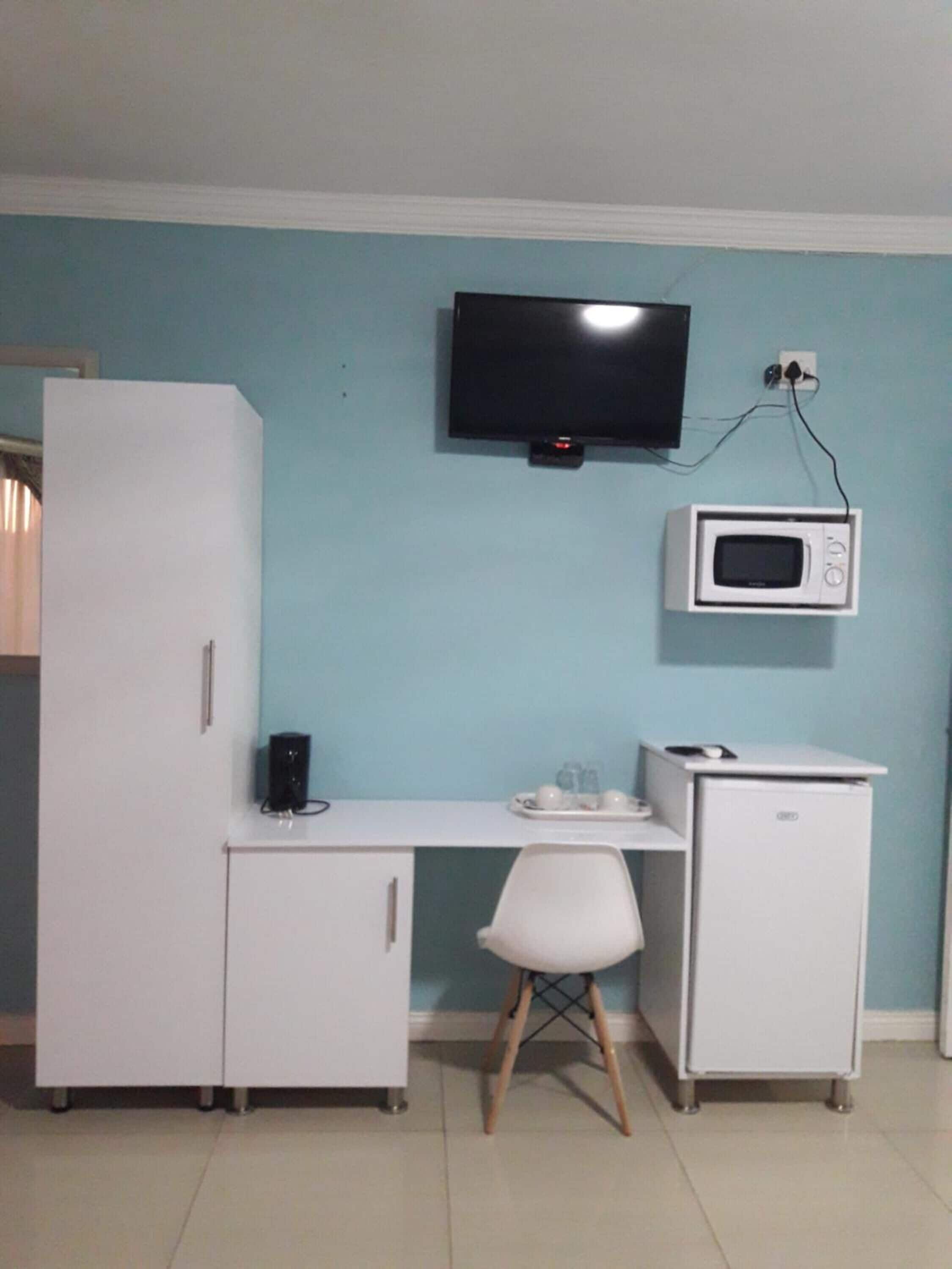 A compact room with a white desk, a chair, a television, a microwave, and a refrigerator.