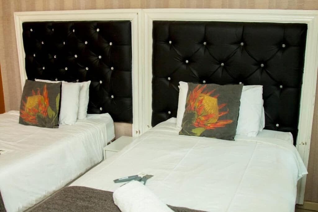 Una habitación de hotel con dos camas, cada una con cabecero negro capitonado y ropa de cama blanca.