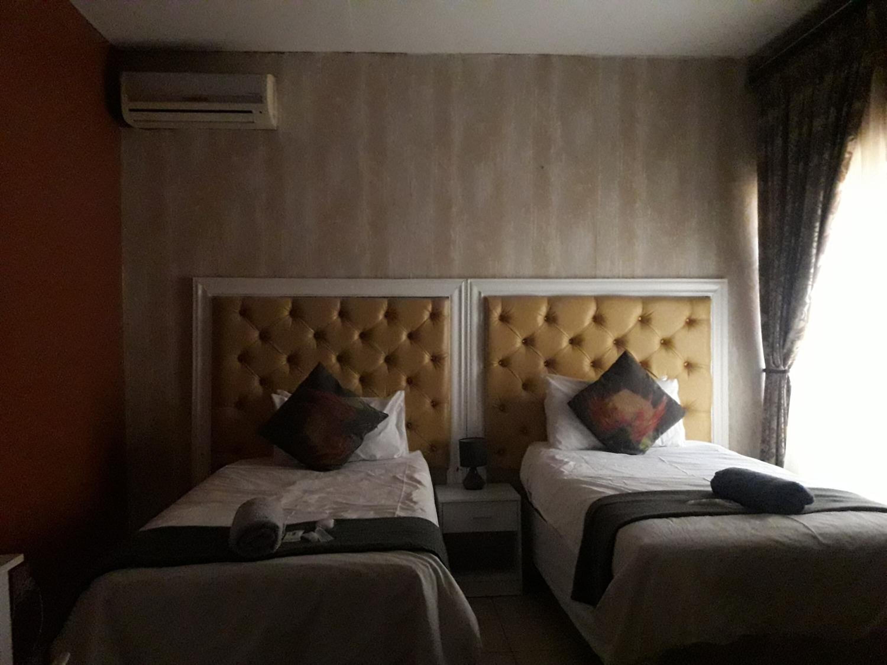 A hotel room with two single beds, each with a headboard, a nightstand, and a lamp.