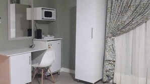 A room with a white desk, a chair, a white wardrobe, a white cabinet, a white microwave, and a patterned curtain.