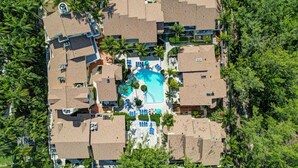 Vista aérea de un resort con varias cabañas, una piscina central y palmeras circundantes.