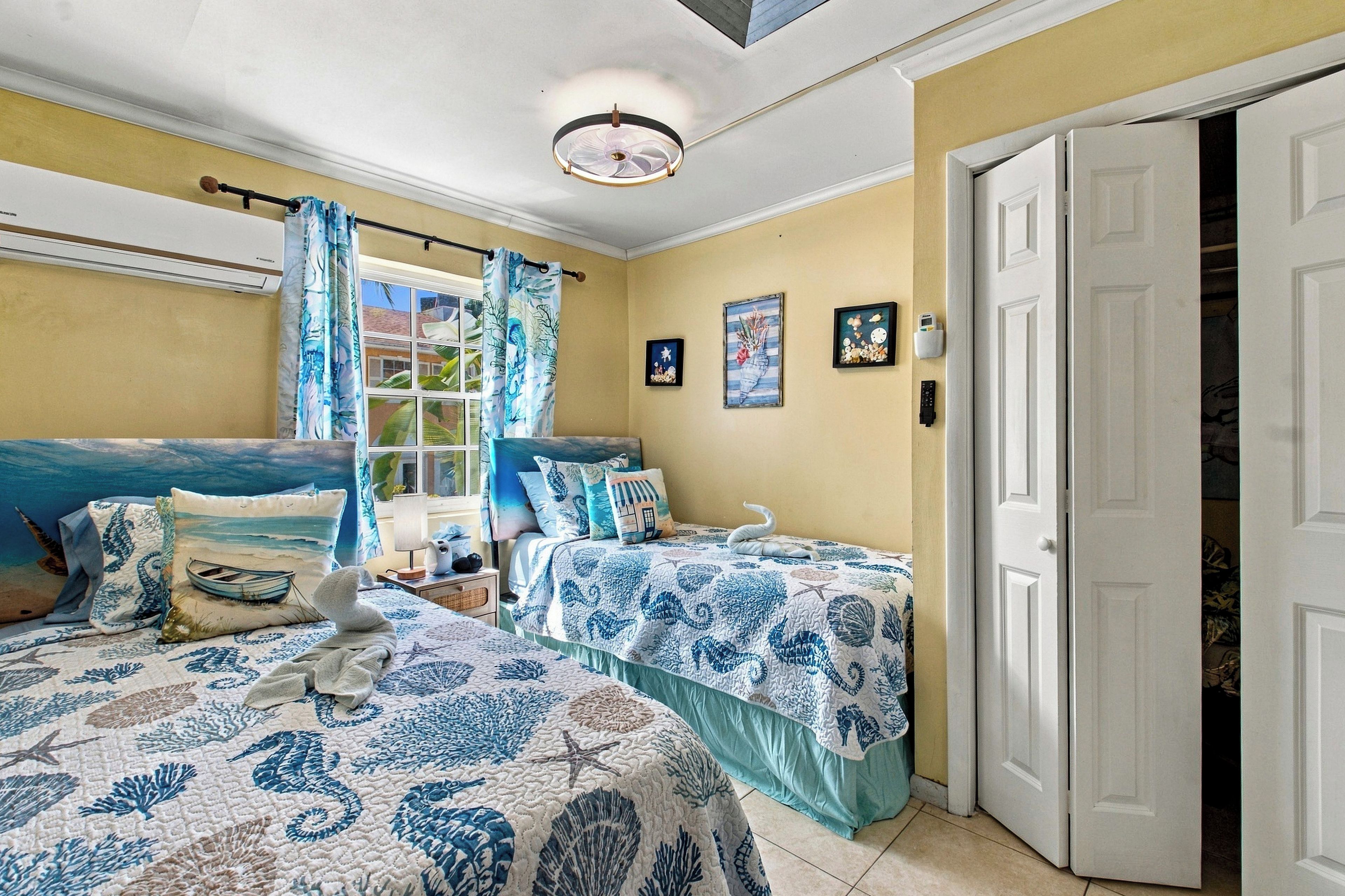 A room with two beds, a window with curtains, a door, and wall decorations.