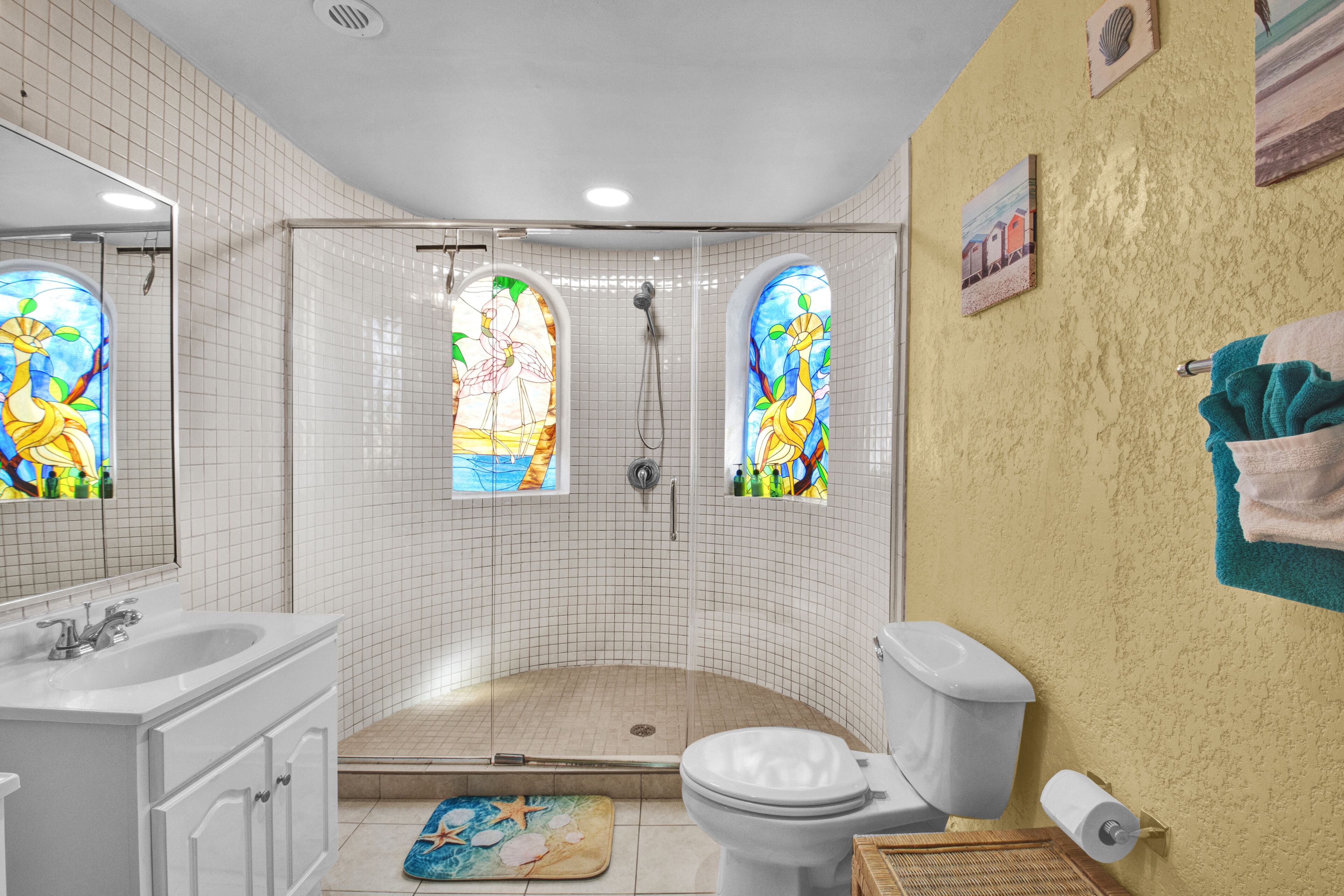 A bathroom with a shower, toilet, sink, and a stained glass window.