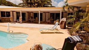 Ein Poolbereich mit Liegestühlen, einem Glastisch und einer überdachten Terrasse.