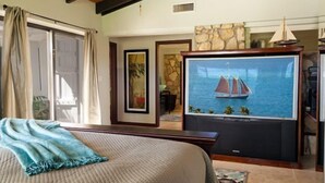 Ein Schlafzimmer mit einem Bett, einem Fernseher, der ein Segelboot auf dem Wasser zeigt, und einer Steinwand.