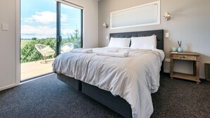 Une chambre avec un grand lit, une table de chevet, une chaise et une vue sur la verdure grâce à une porte coulissante.