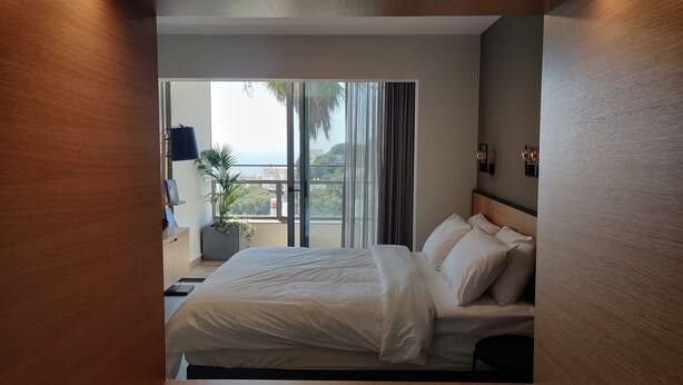 Camera d'albergo moderna con un letto grande, vista sulla città e un balcone con una pianta.