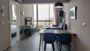 Una stanza moderna e luminosa con zona pranzo, divano, TV e ampie finestre che offrono vista sulla città.
