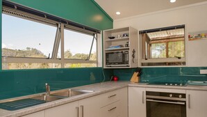 A modern kitchen with a sink, microwave, oven, and a window with a view of the outdoors. - Coro Beach Haven - Hahei Holiday Home (Hahei)