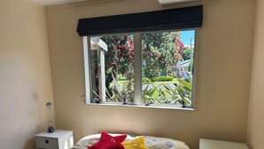 A bedroom with a bed, a bedside table, a nightstand, and a window with a view of a garden. - Coro Beach Haven - Hahei Holiday Home (Hahei)