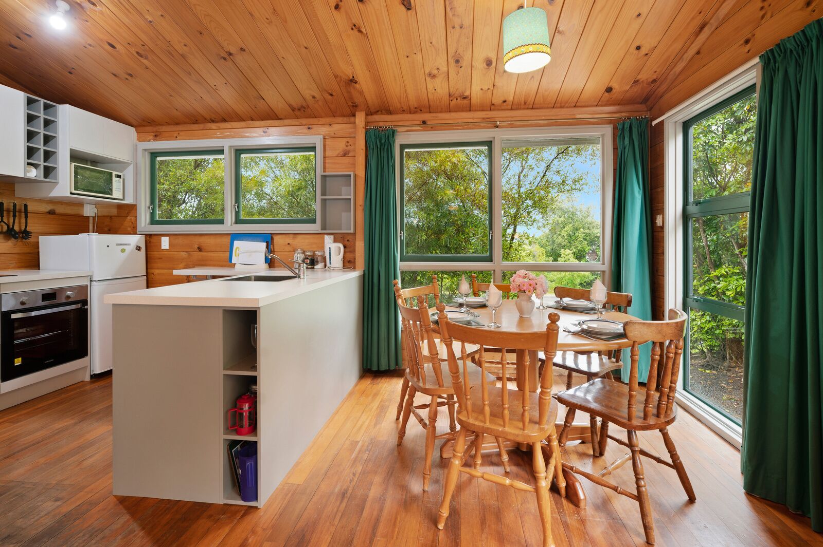A modern kitchen with wooden cabinets, a central island, and a dining area with wooden chairs.