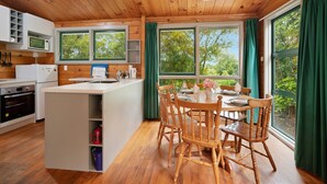 A modern kitchen with wooden cabinets, a central island, and a dining area with wooden chairs. - Little Lockwood - Kuratau Bach (Kuratau)